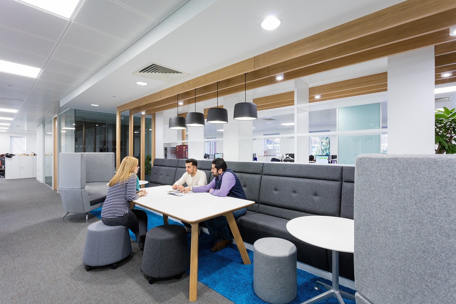 Two men and one woman seated around a table in the Clinigen office meeting area with bright, modern lighting