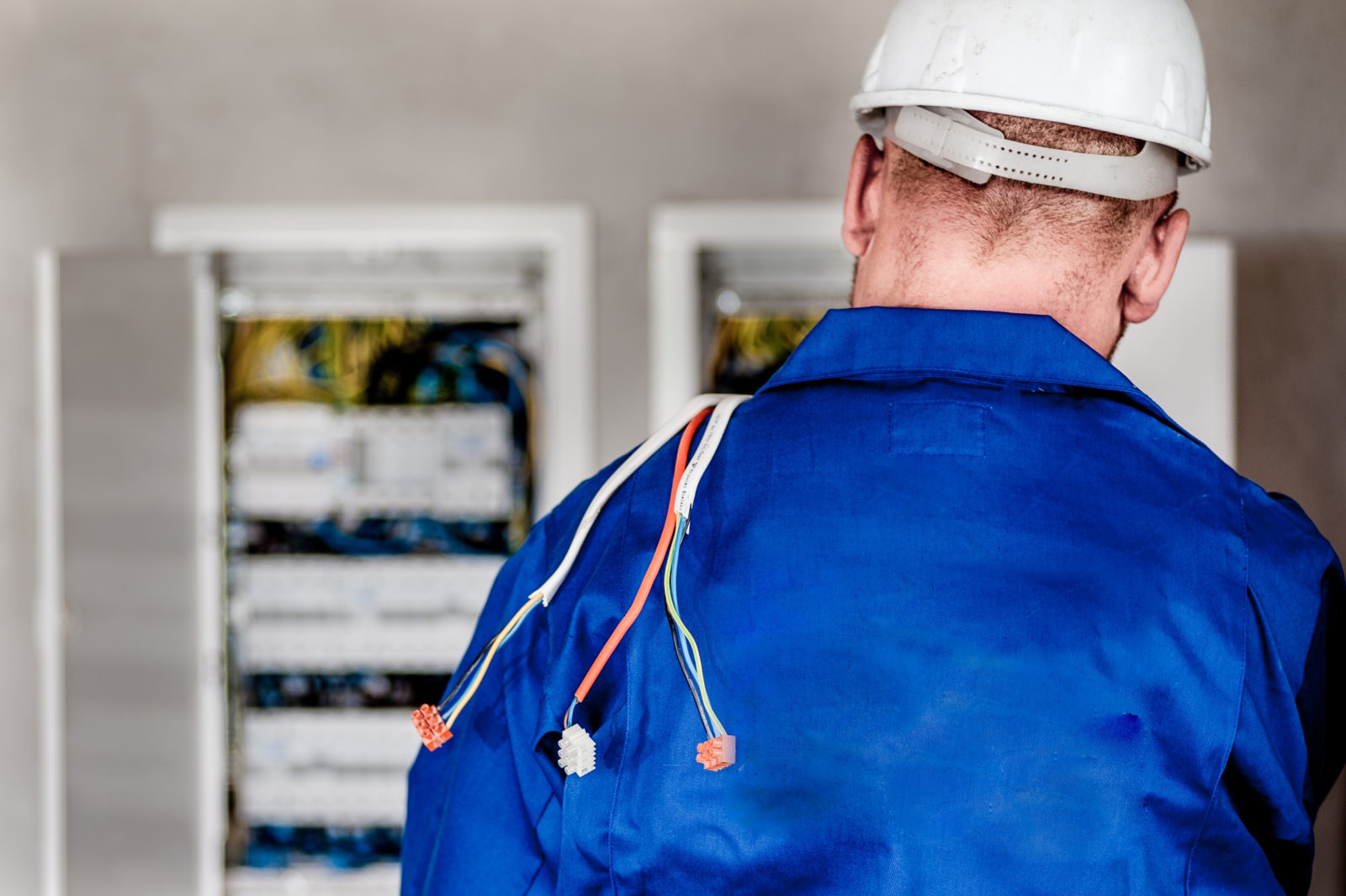 Man wearing a work hat inspecting electrical wires with cables over his shoulder