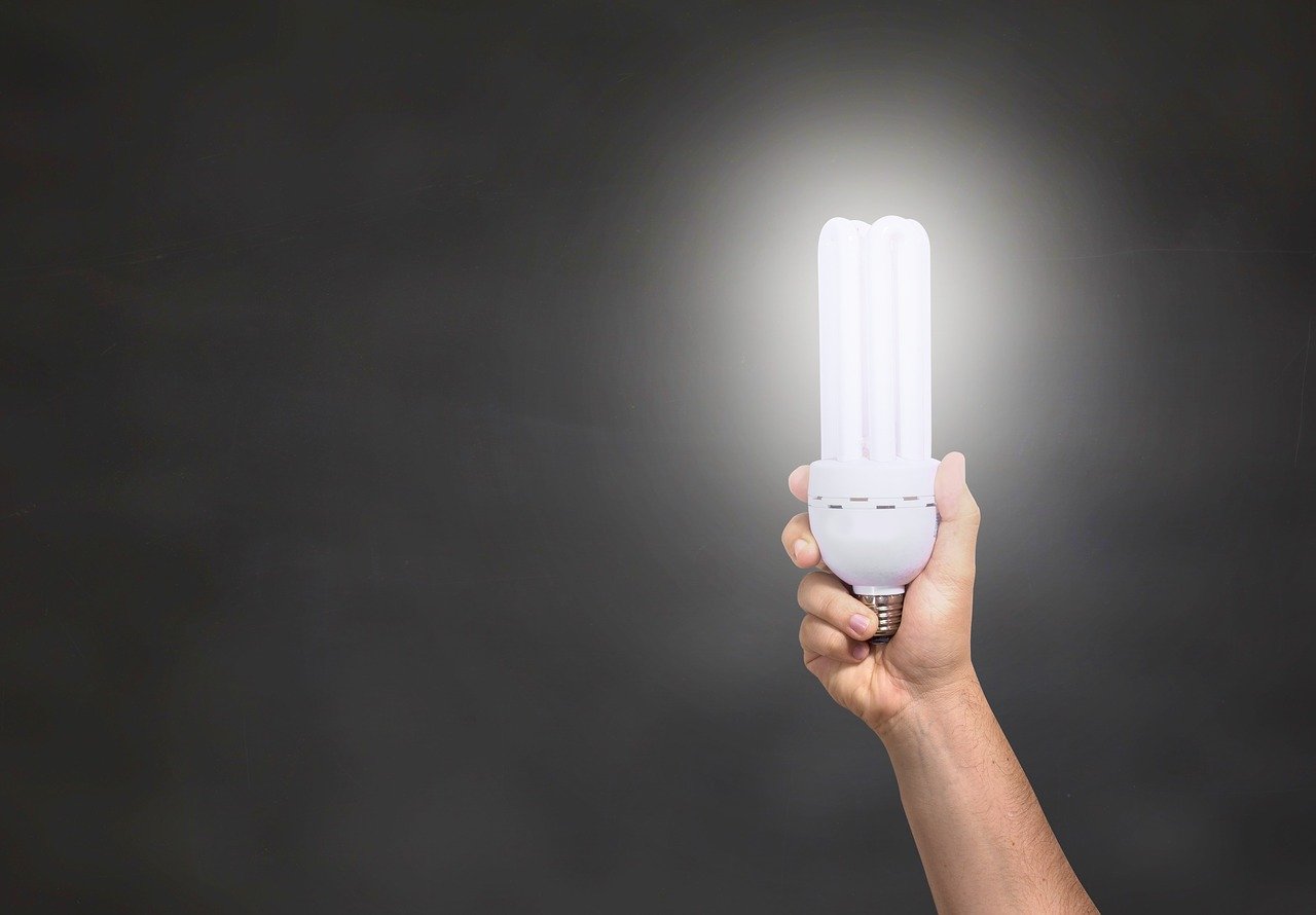 Hand holding a glowing LED lightbulb against a black background